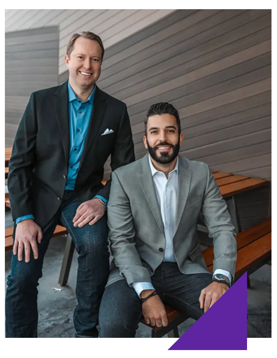 Two men in suits are sitting next to each other on a bench.