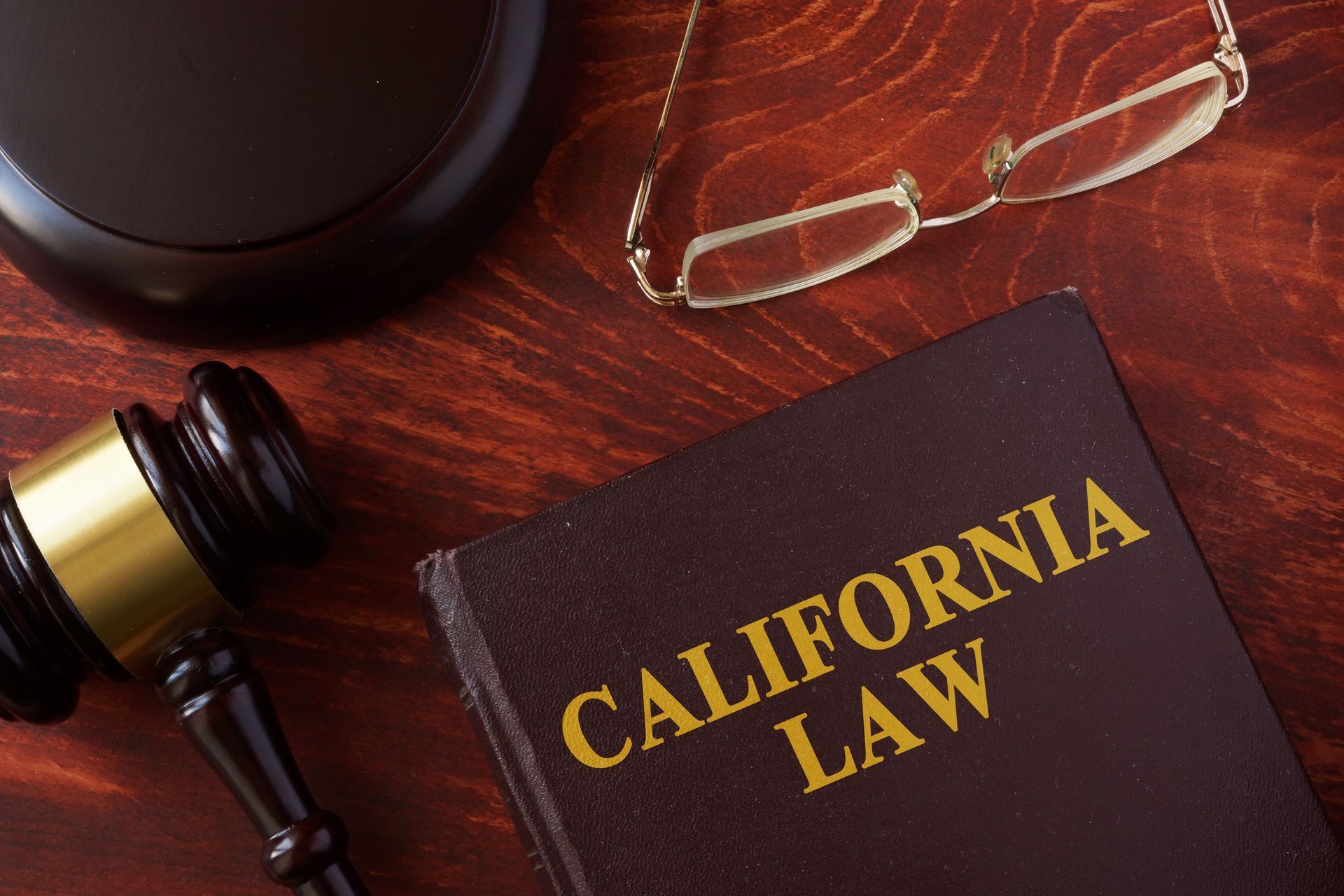 Gavel, California Law book, and eyeglasses on a wooden table.