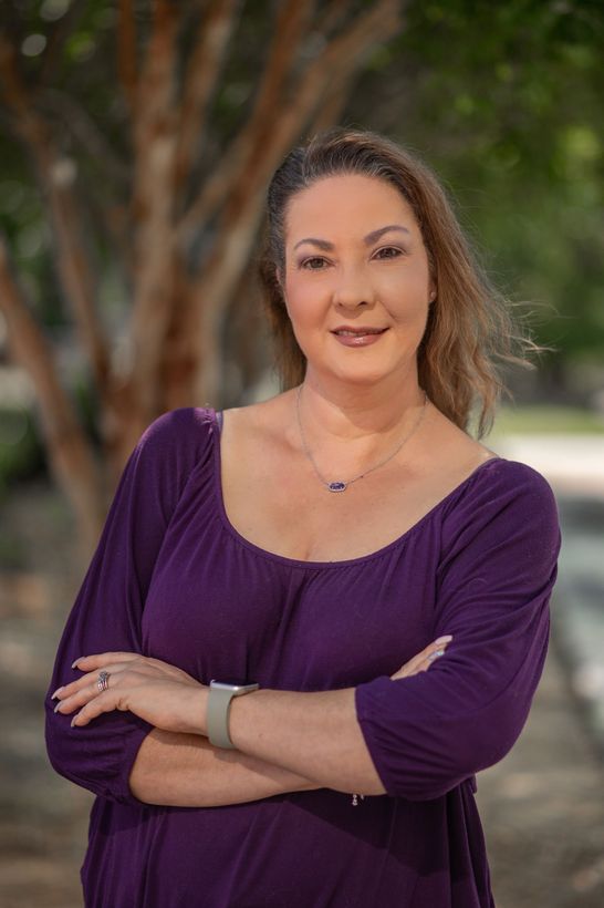 A woman is sitting at a desk with a laptop and a vase of flowers.