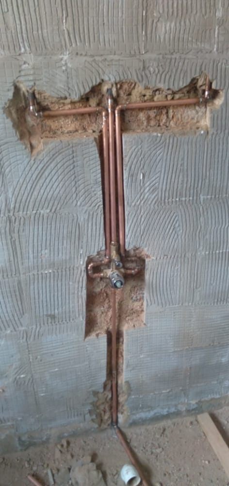 Bathroom wall showing copper plumbing pipes exposed before being tiled over