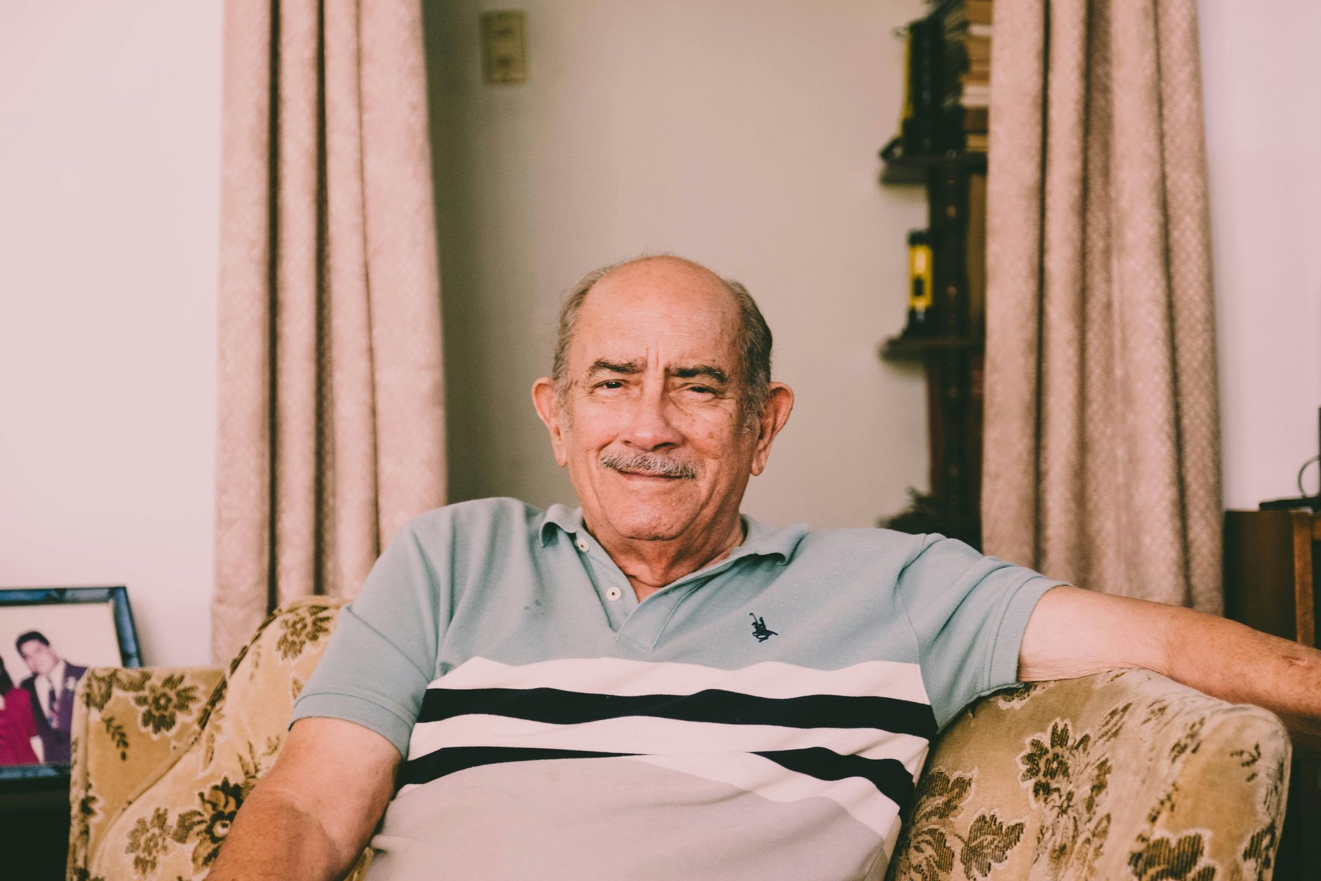 An elderly man is sitting in a chair in a living room.