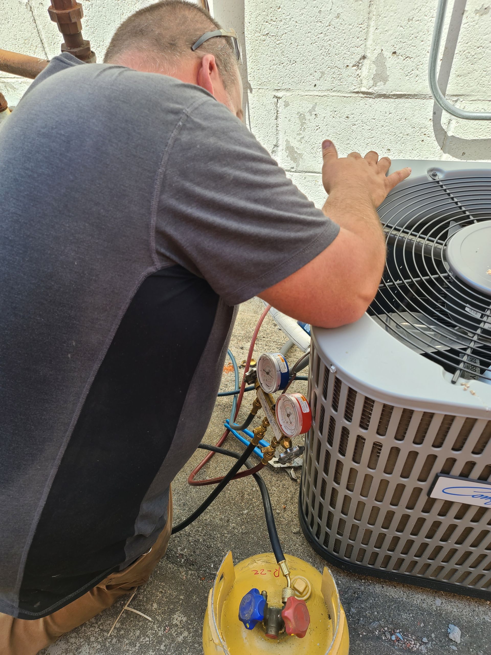 A man is kneeling down next to an air conditioner.