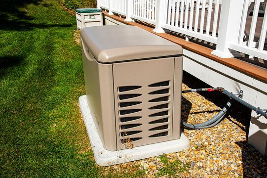 A generator is sitting on the side of a house next to a deck.