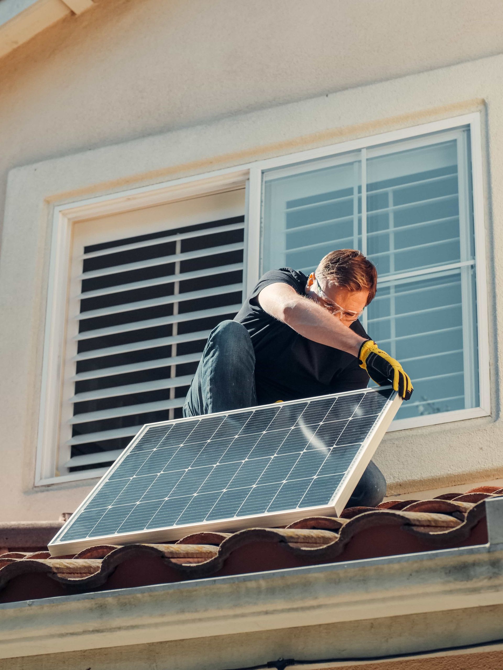 A man is installing a solar panel on the roof of a house.