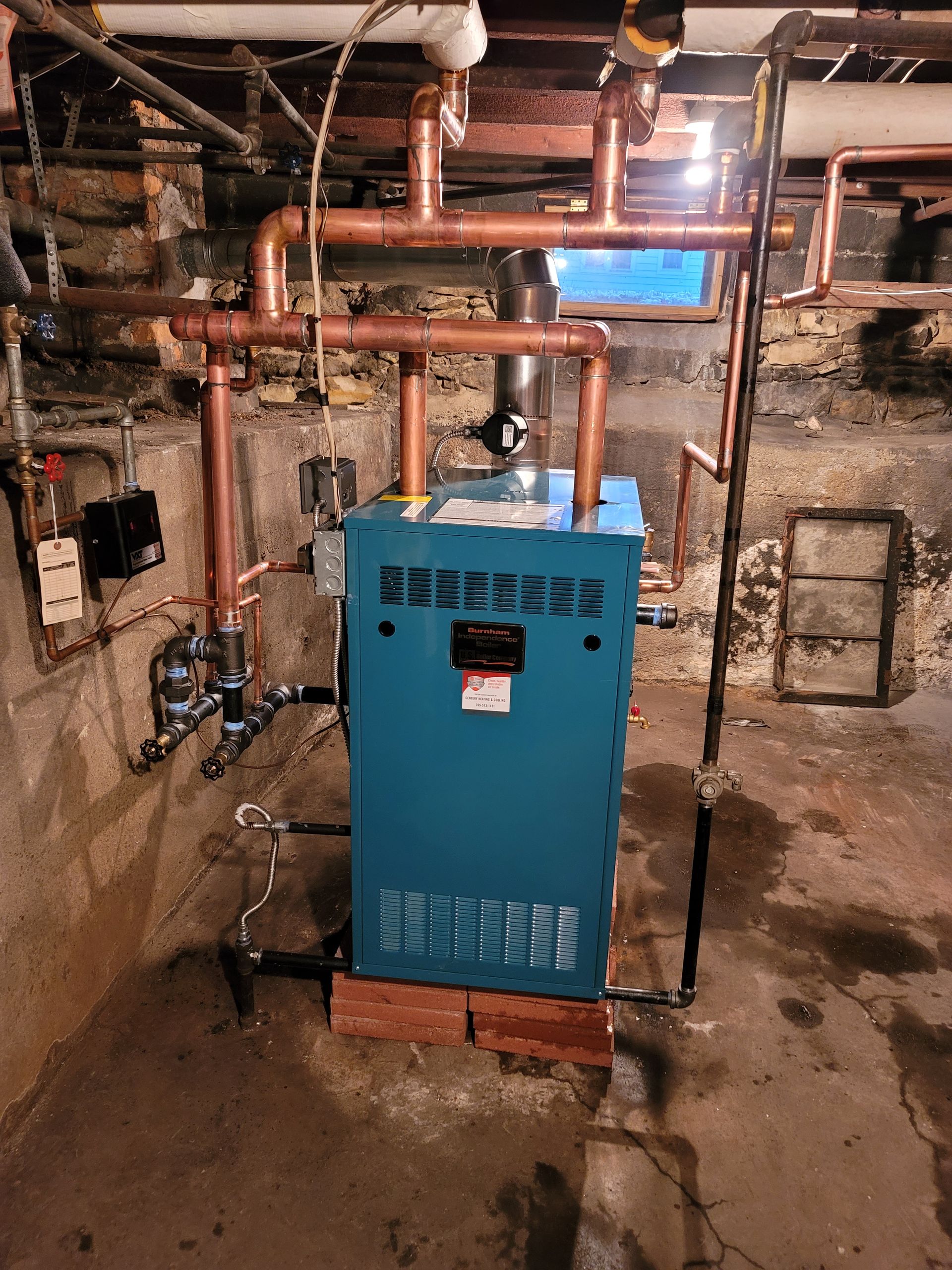 A blue boiler is sitting in a basement next to copper pipes.
