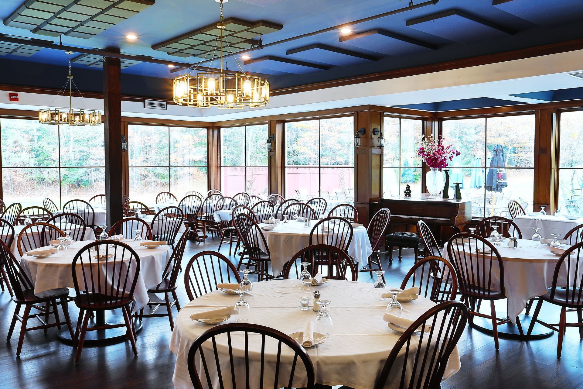 A large dining room with tables and chairs and a piano.