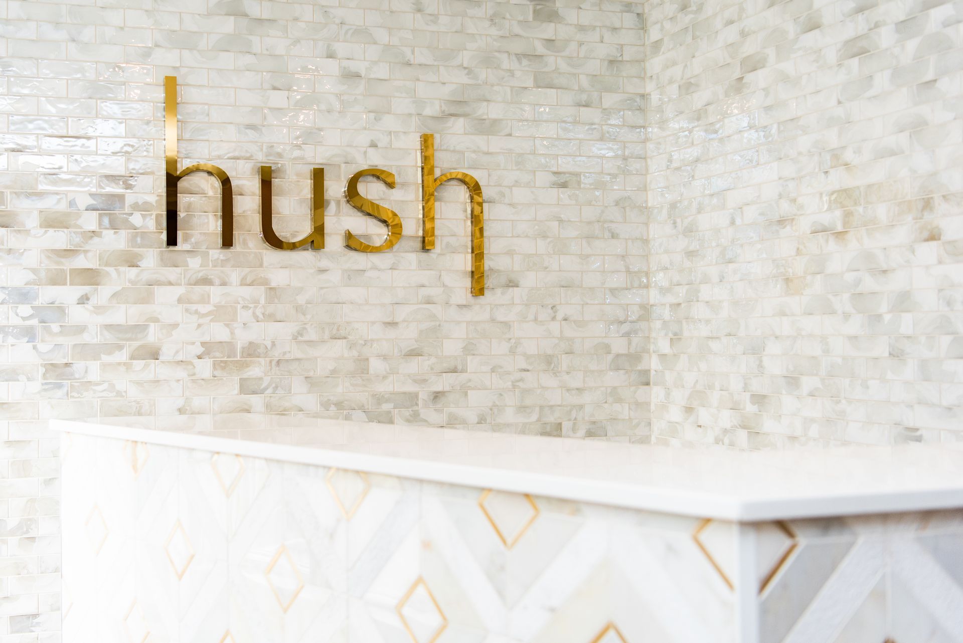 the word hush is written in gold on a white brick wall .