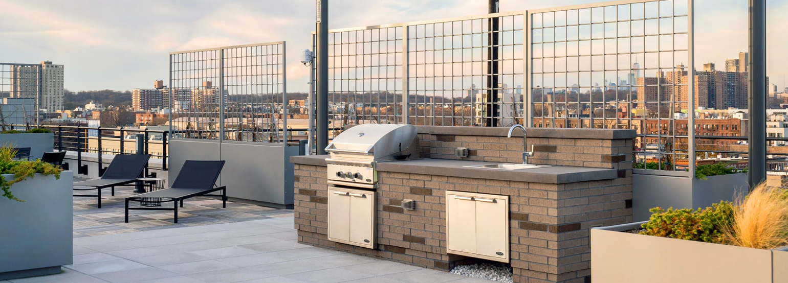 a rooftop kitchen with a grill , sink and chairs .