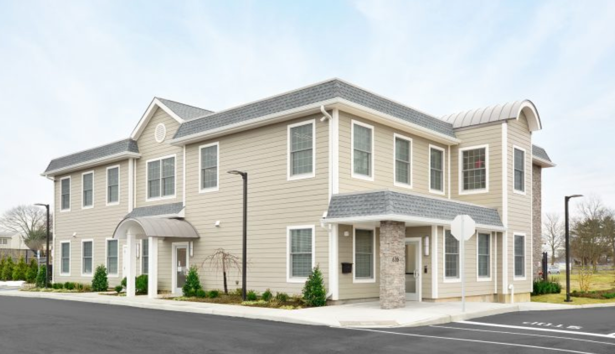 A large beige building with a lot of windows and a parking lot in front of it.