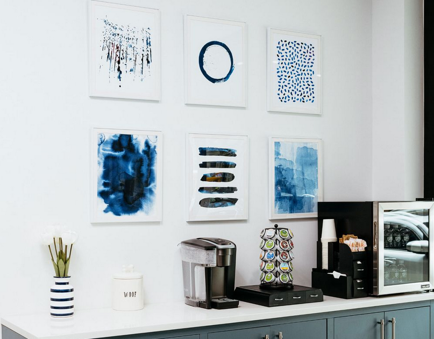 A kitchen with a coffee maker , microwave , and paintings on the wall.