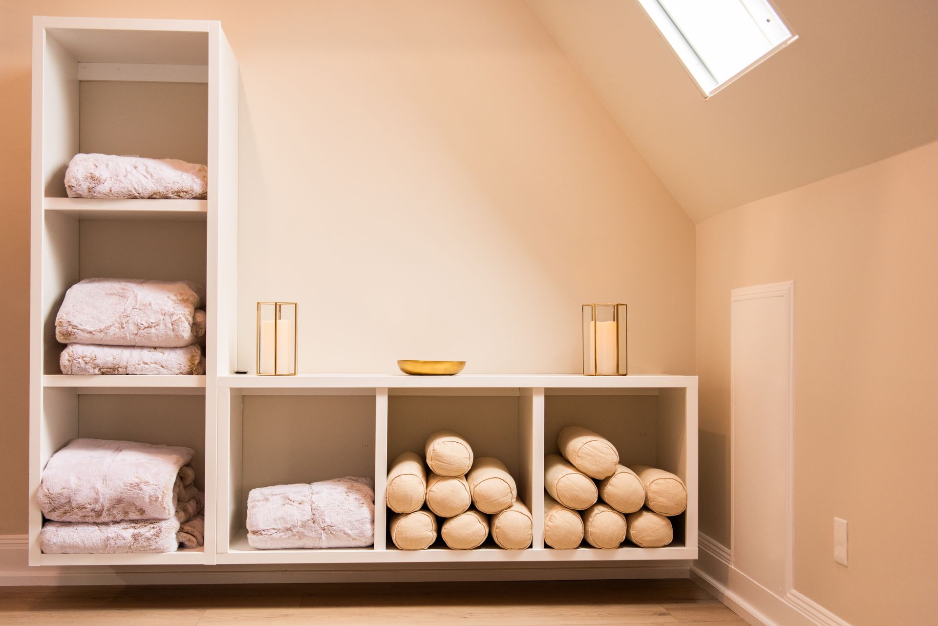 a room with a shelf filled with towels and pillows under a skylight .