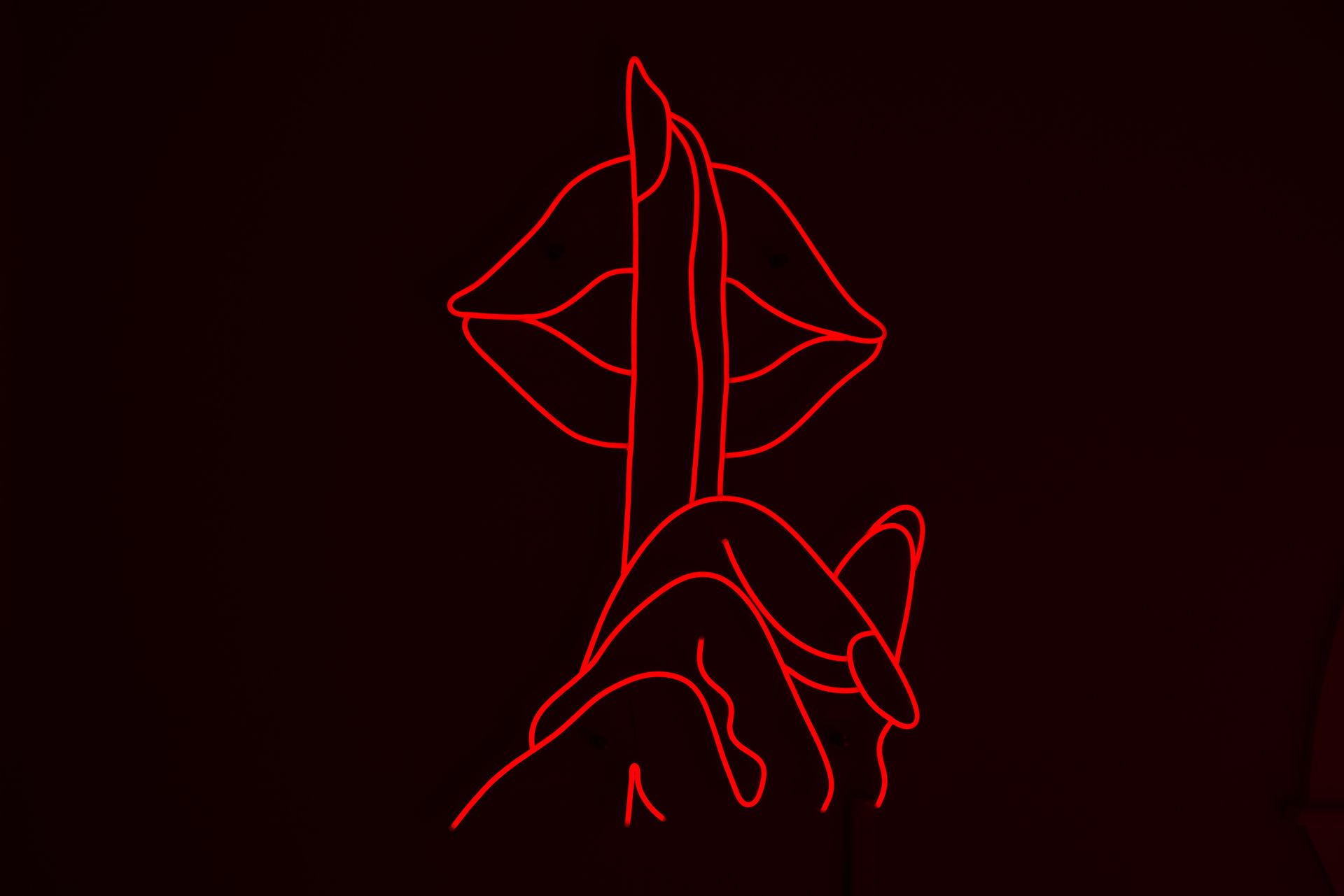 a neon sign of a person holding their finger to their mouth .