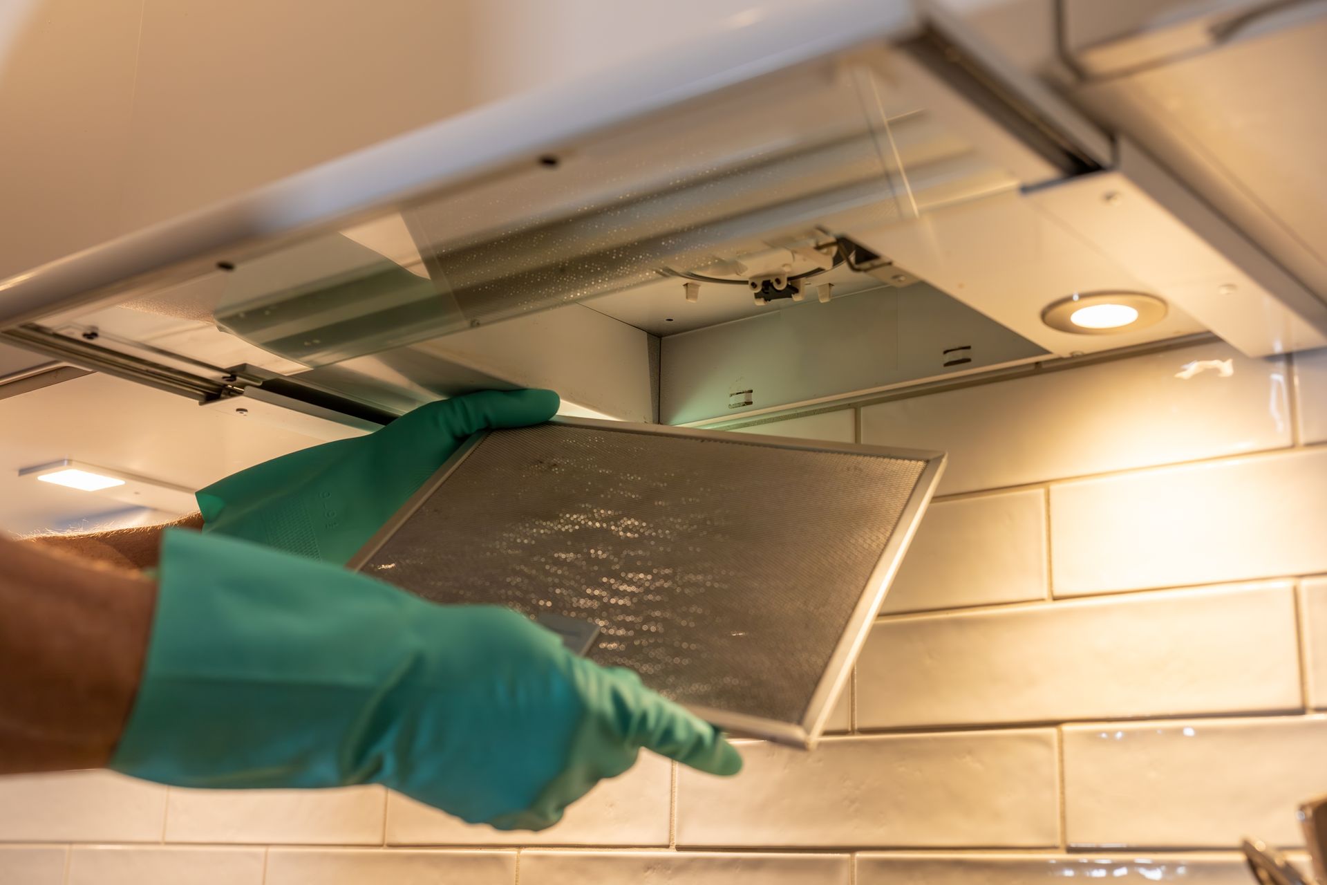 A person wearing green gloves is cleaning a kitchen hood filter.