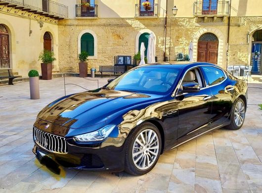 Una Maserati Ghibli nera è parcheggiata davanti a un edificio.