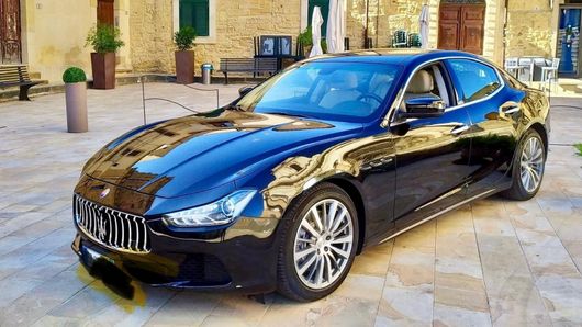 Una Maserati Ghibli nera è parcheggiata davanti a un edificio.