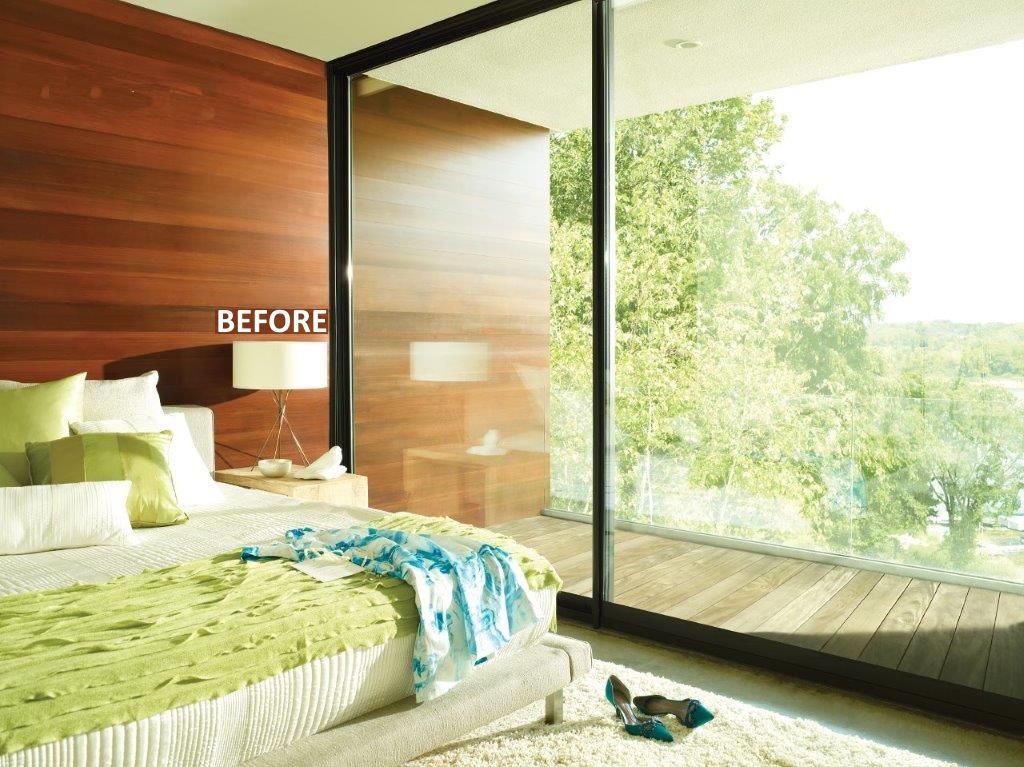 Bedroom with wood paneling, large window overlooking trees, bed with green and white linens.