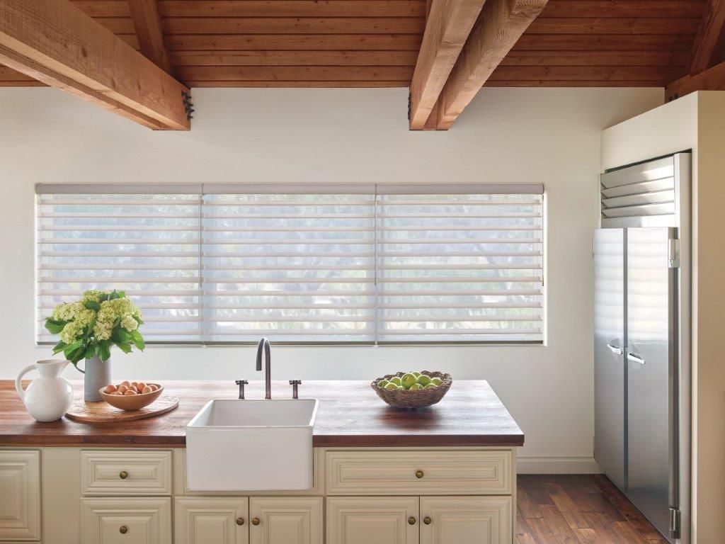 Kitchen with white cabinets, butcher block counters, and layered window shades.