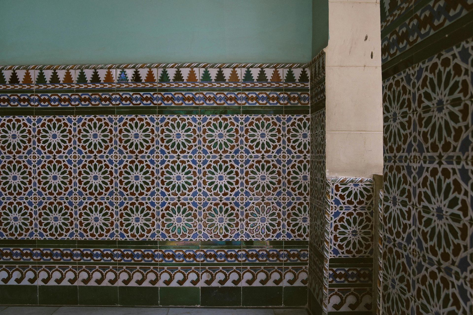 Carrelage mural décoratif en mosaïque à motifs géométriques bleus, marron et blancs, avec une bande verte.