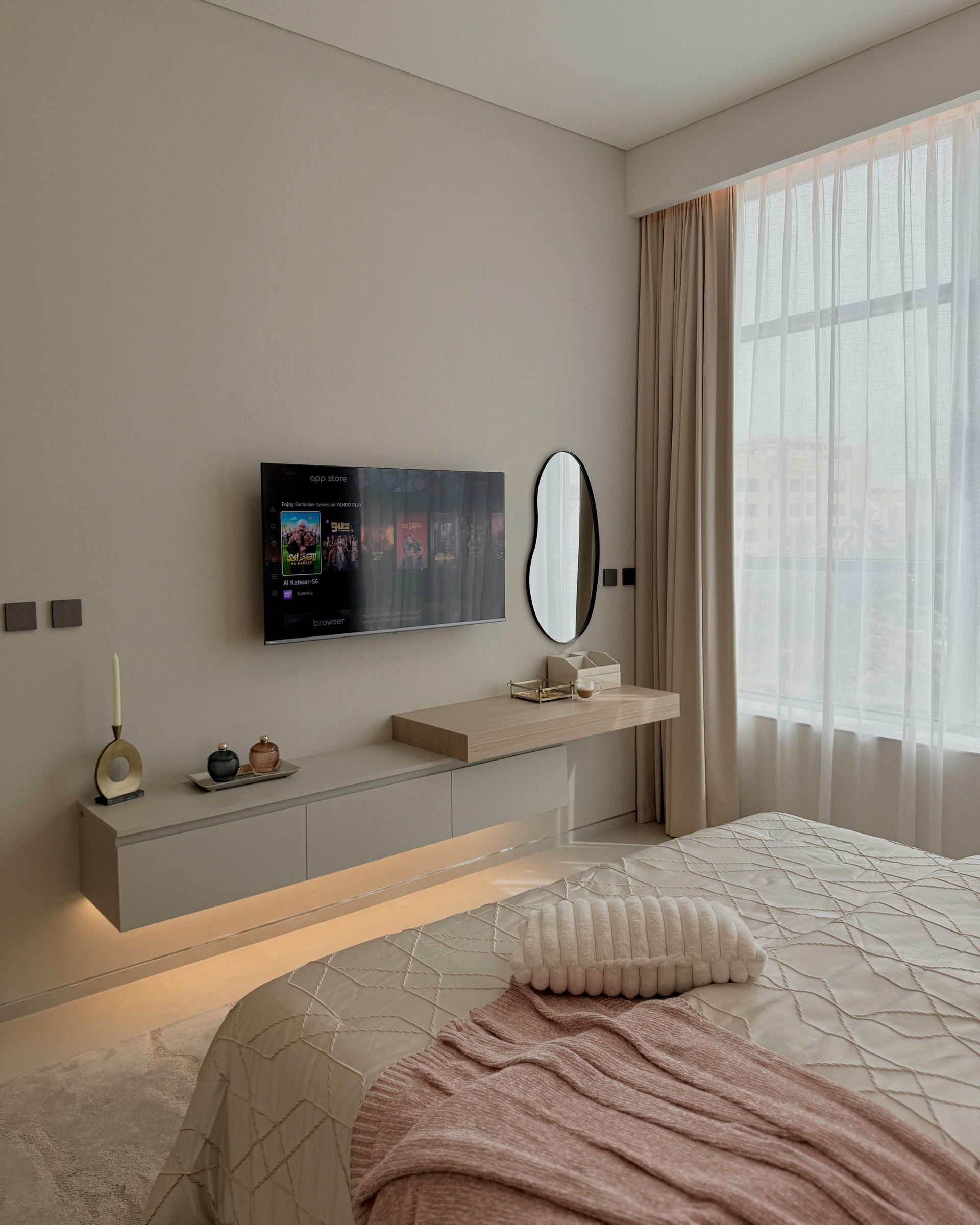 Une chambre avec une télévision flottante, une coiffeuse et un lit, le tout dans des tons neutres.