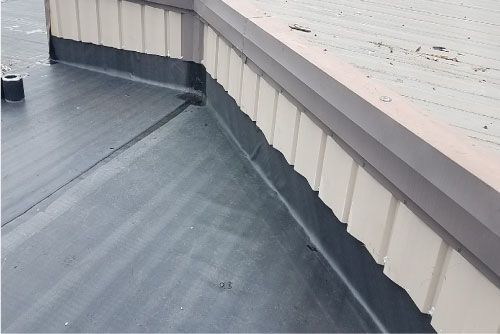 Close-up of a flat roof with dark, possibly sealed surface, meeting building trim.