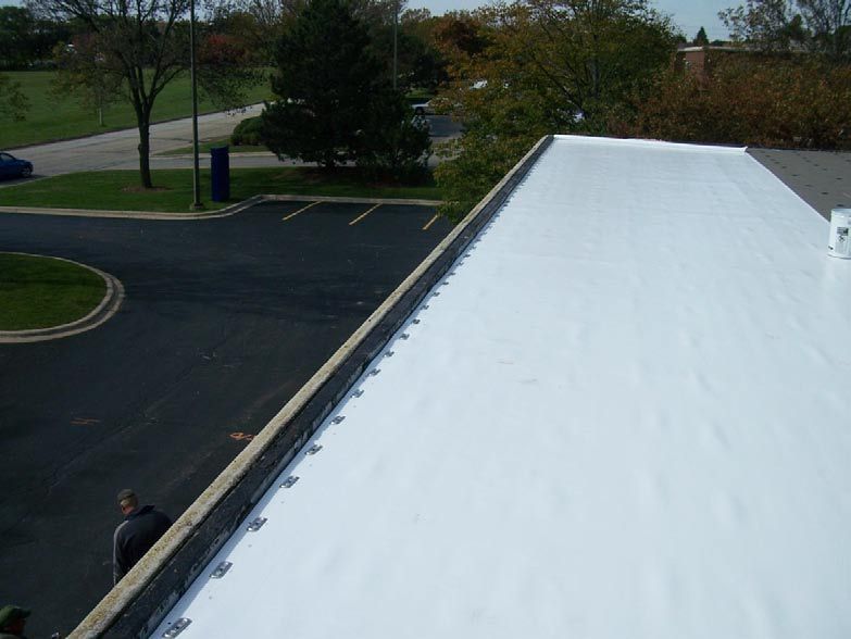 White commercial flat roof with black edge, overlooking a parking lot and trees.