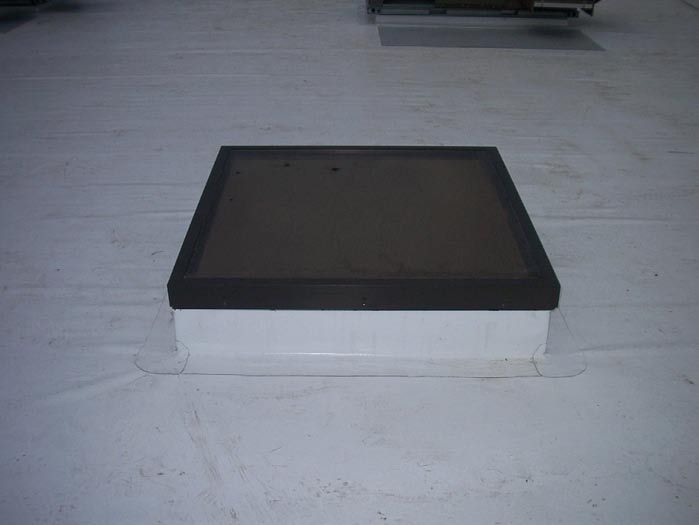 Square skylight with dark glass and white trim on a white roof.