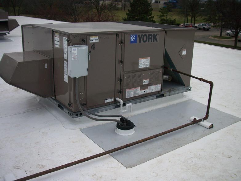 Rooftop air conditioning unit, York brand, brown and gray, on a white roof, with piping and electrical box.