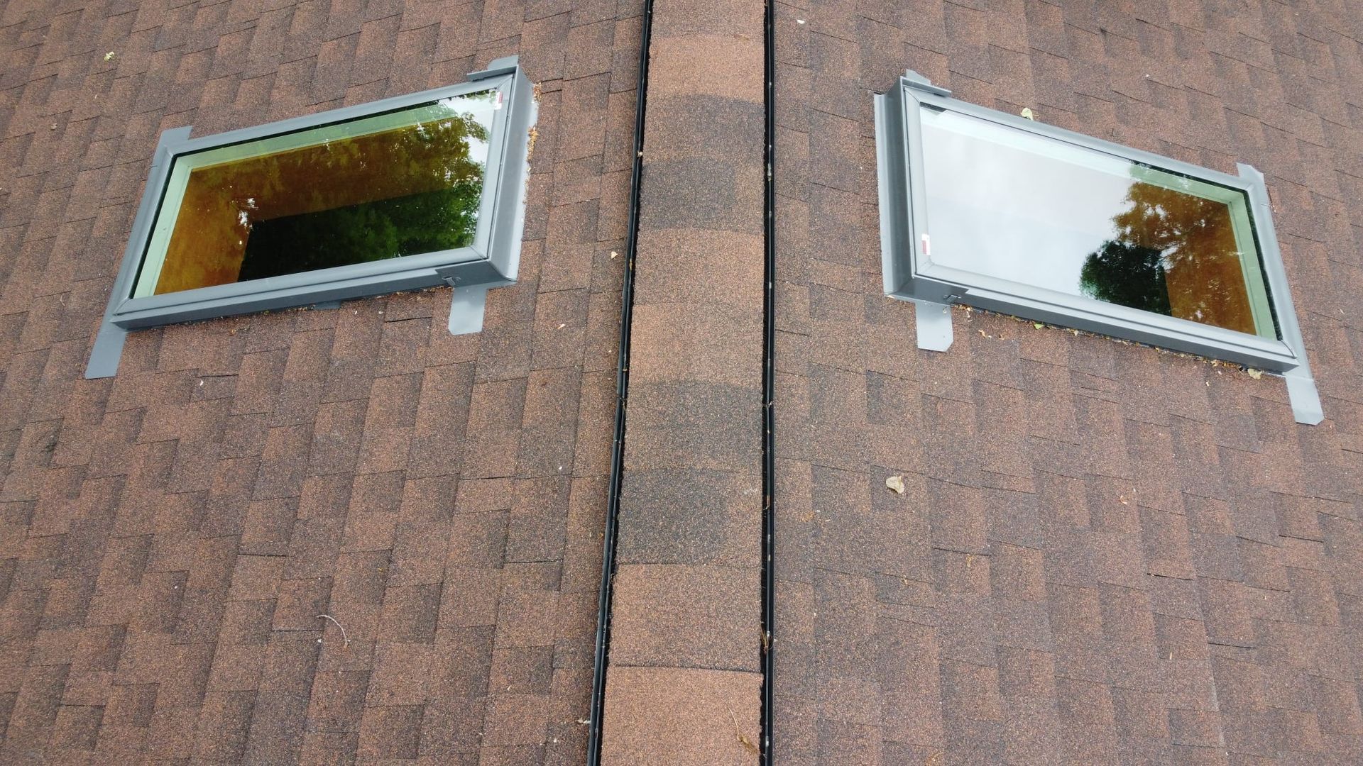 Two rectangular skylights on a brown shingled roof, next to a vertical seam.