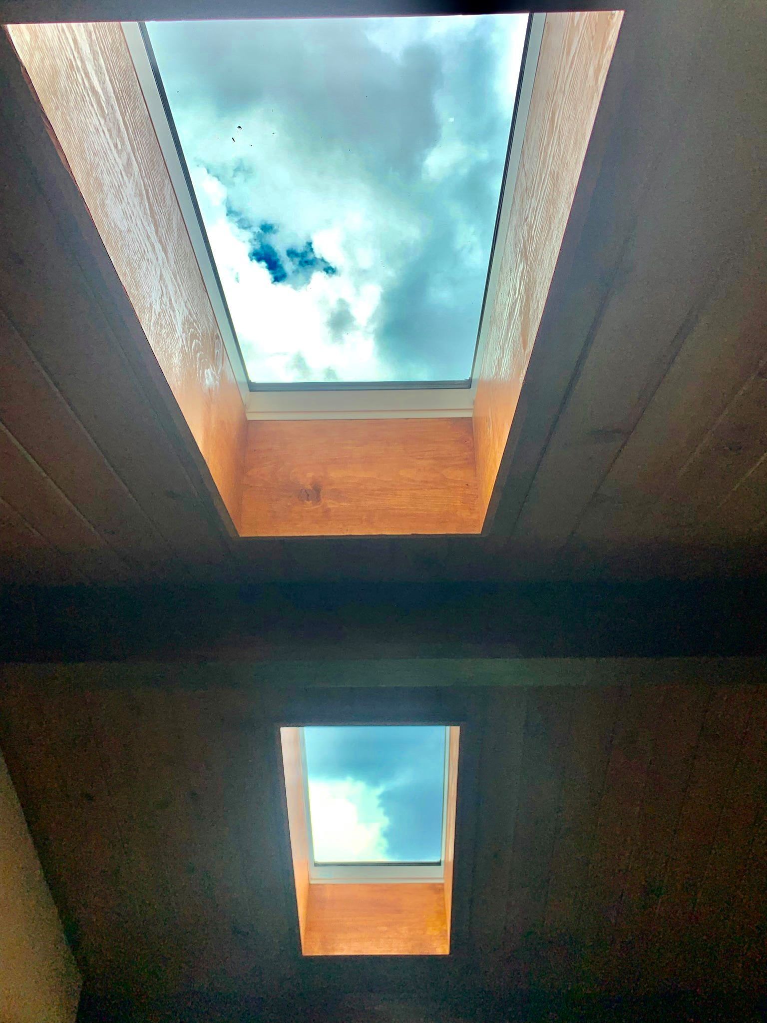 Two skylights in a wooden ceiling, revealing a cloudy, blue sky.