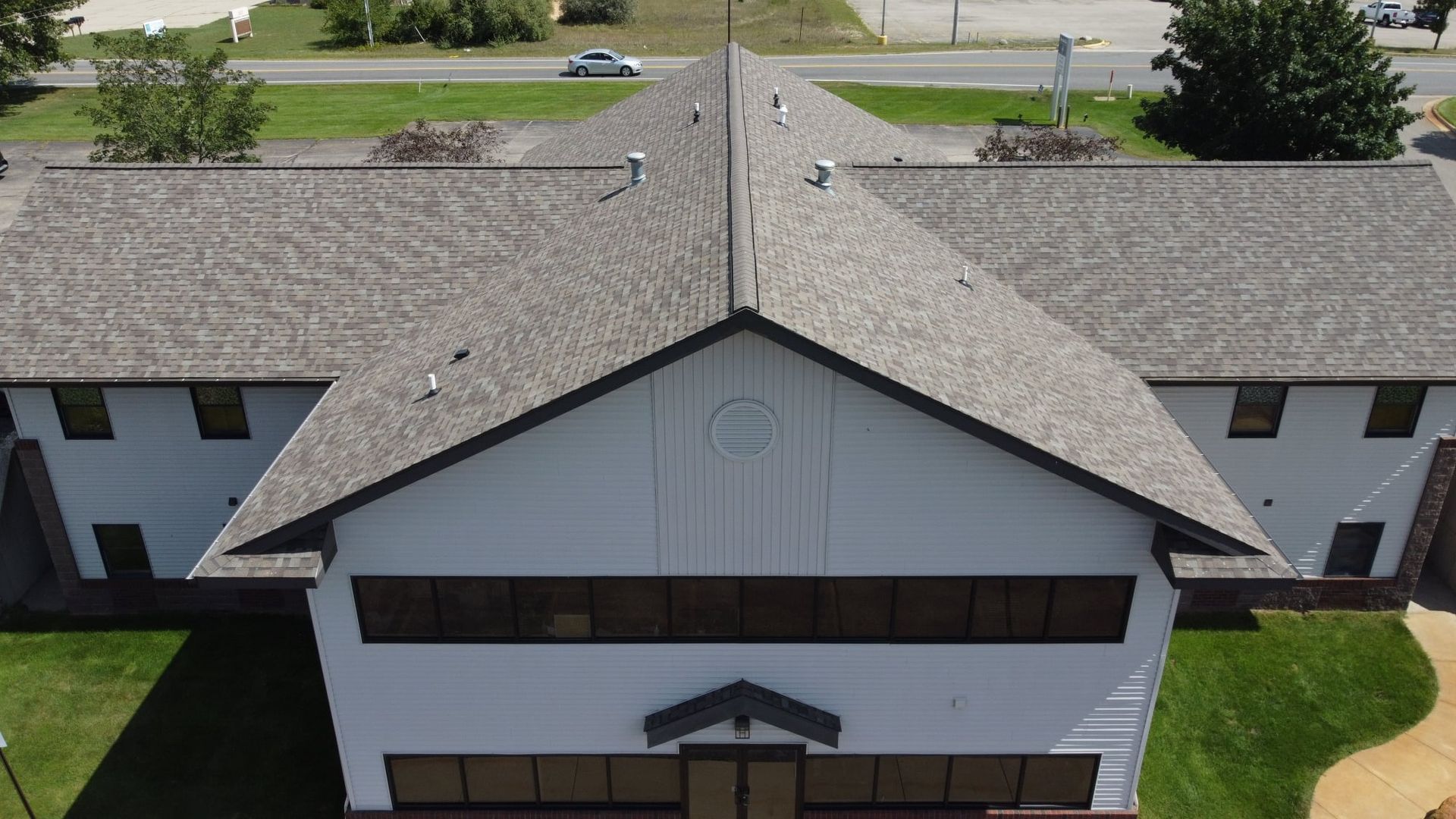 Building with a gray roof and white facade, surrounded by green grass and trees.