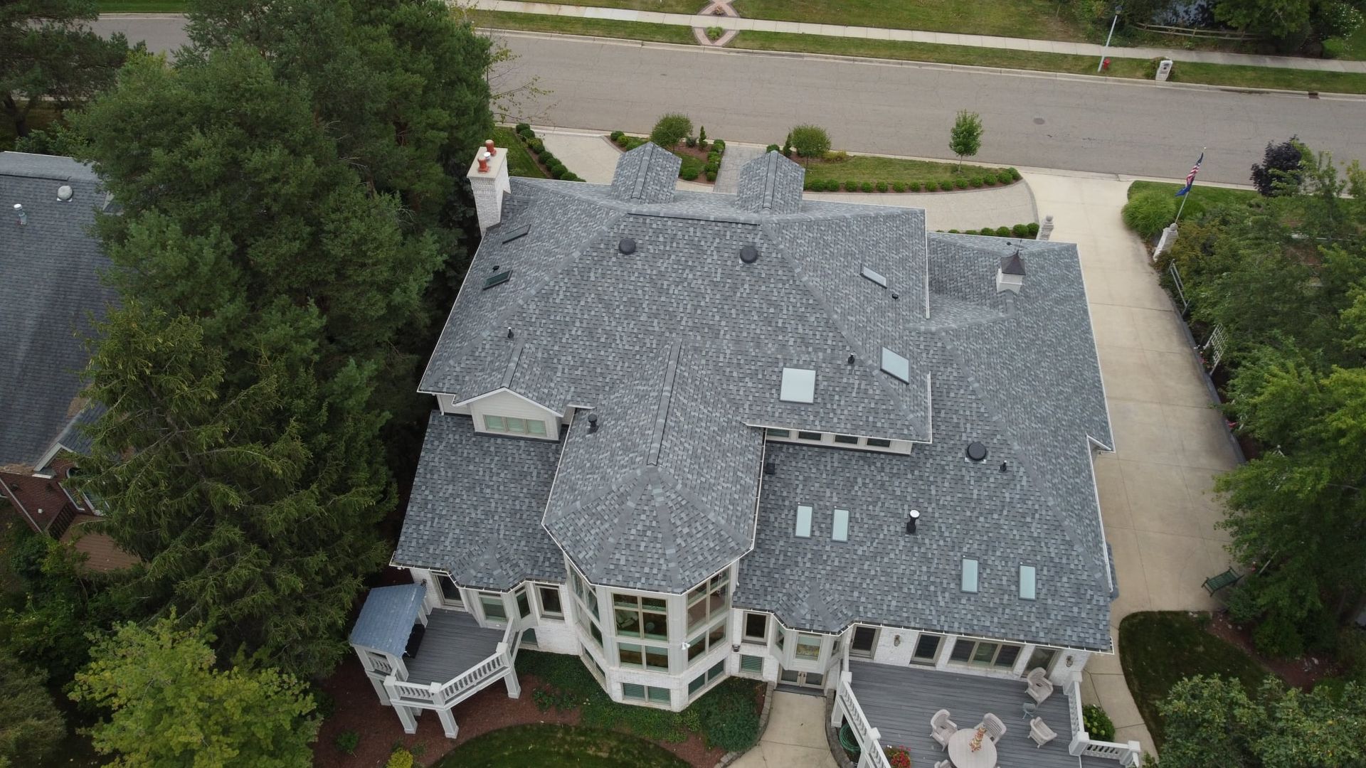 Aerial view of a large house with a gray roof and white siding, surrounded by trees and a driveway.