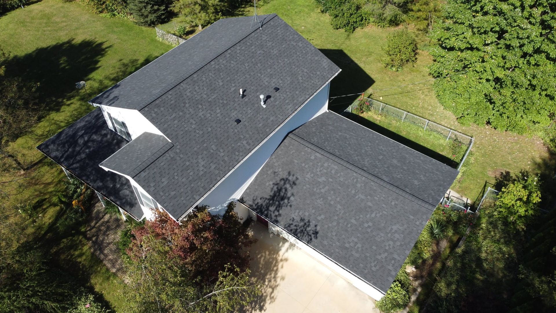 Overhead view of a white house with a dark gray shingled roof, surrounded by green grass and trees.
