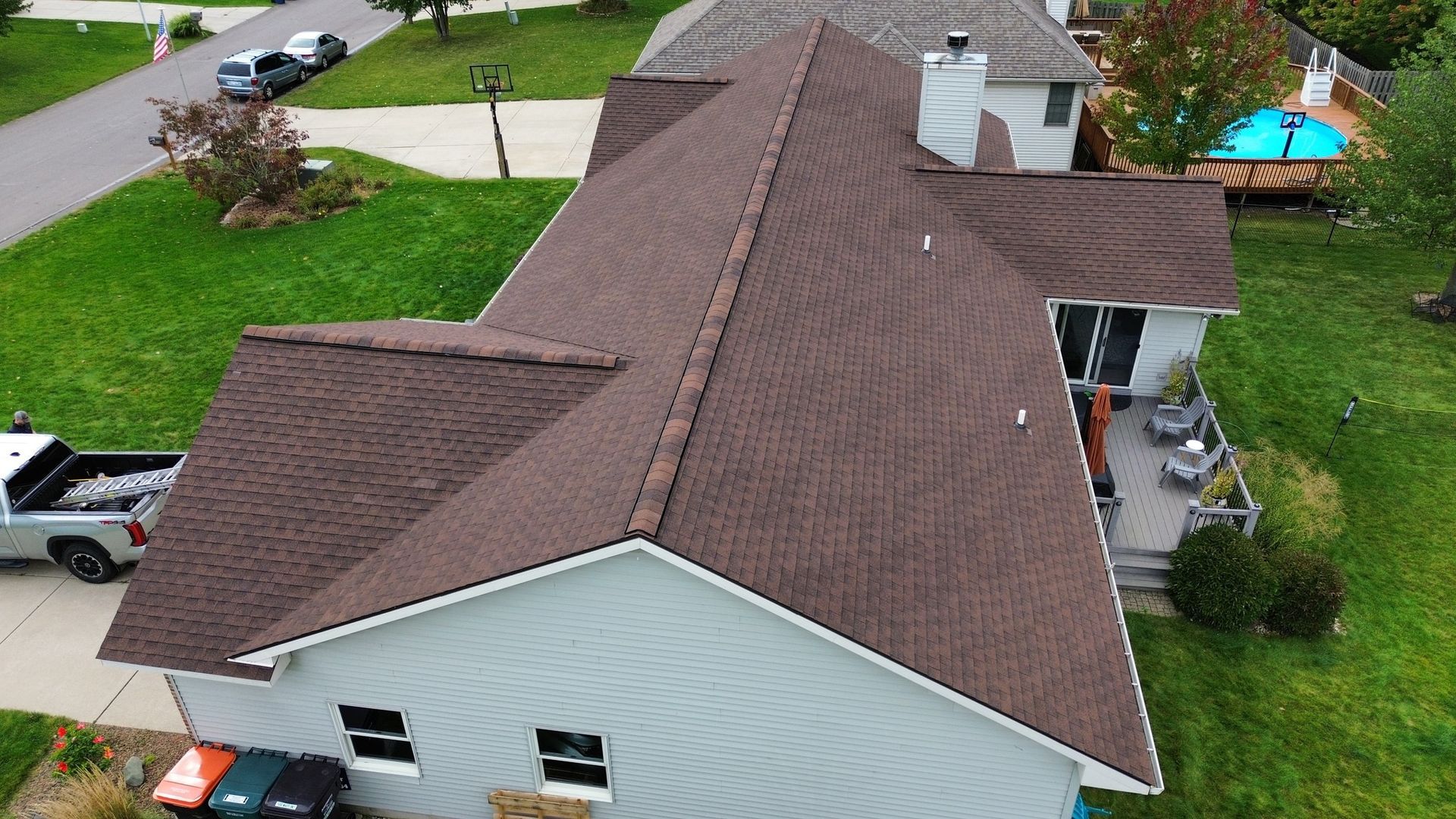 Aerial view of a house with a brown roof and a white exterior, set in a green lawn.