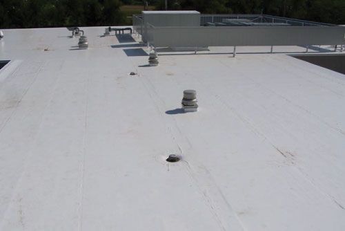 White, flat commercial roof with several vents and HVAC equipment; sunlight.