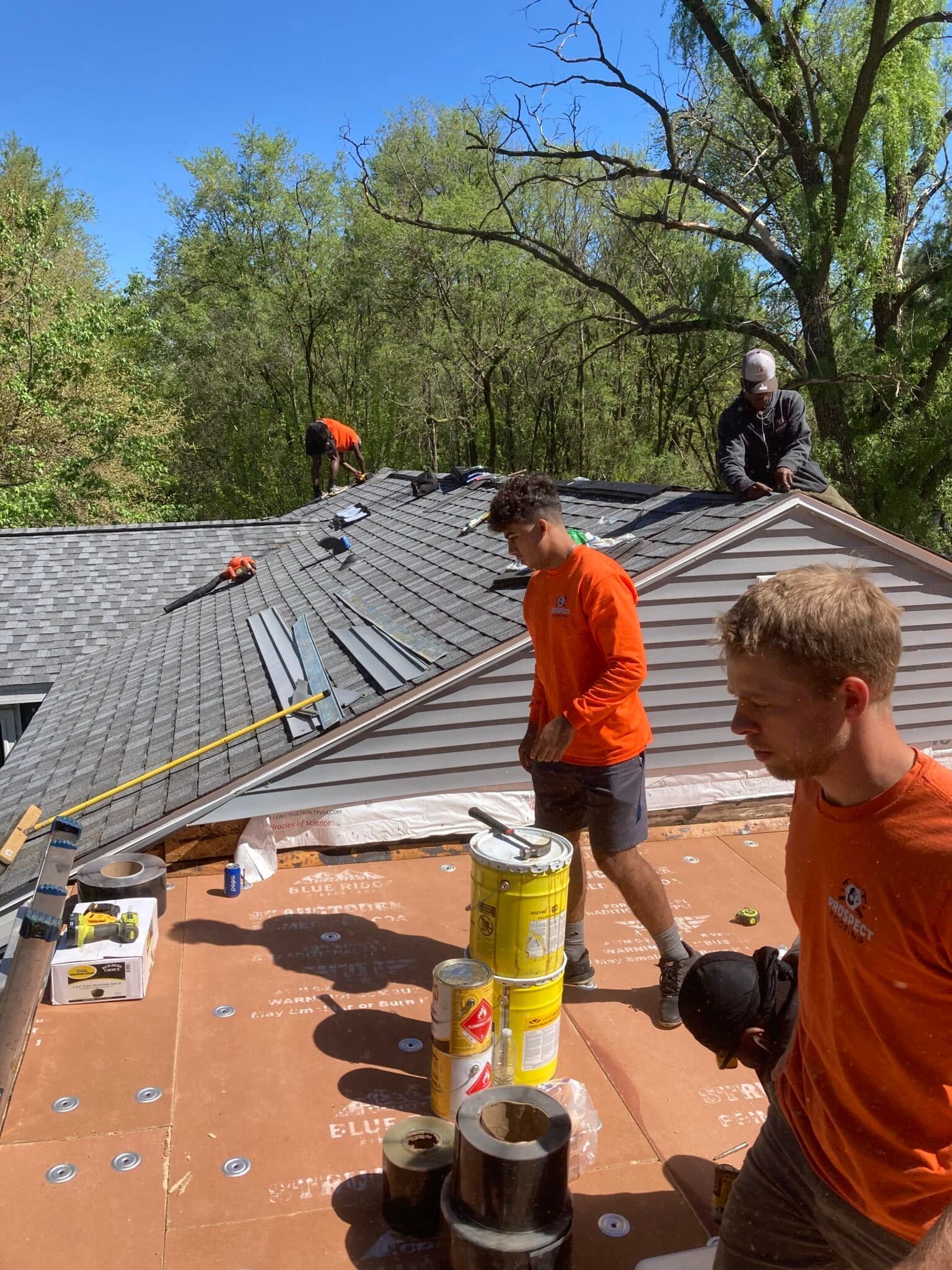 Roofers in orange shirts working on a house roof on a sunny day.