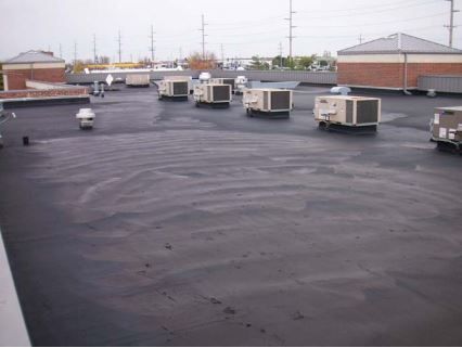 Flat commercial roof with HVAC units. Dark surface with water marks, overcast sky.