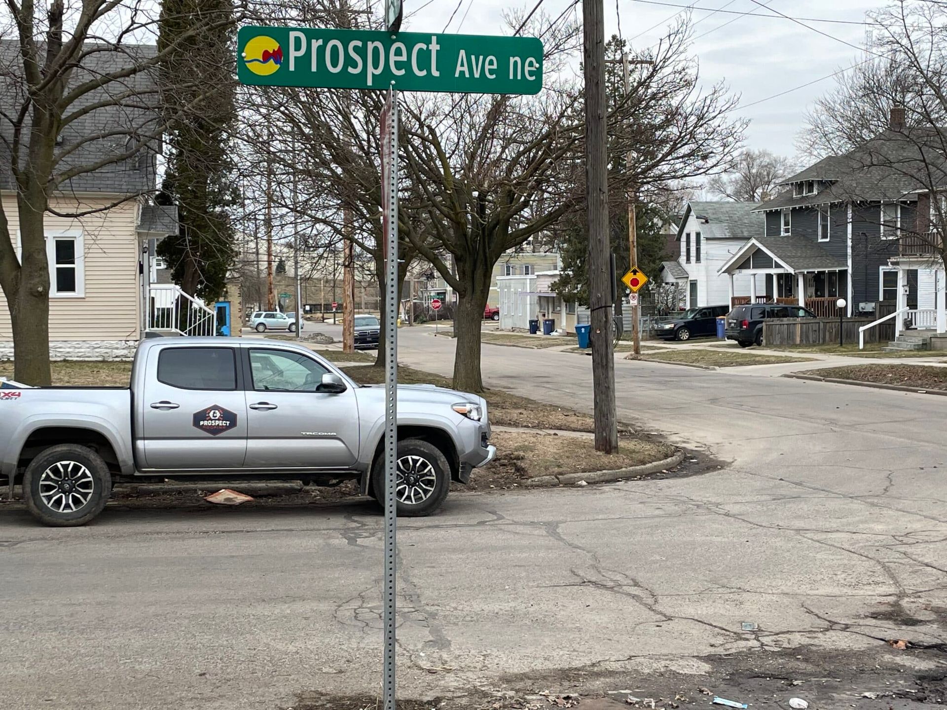 Street sign at the corner of Prospect Ave NE. A gray pickup truck is parked on the street. Houses in the background.