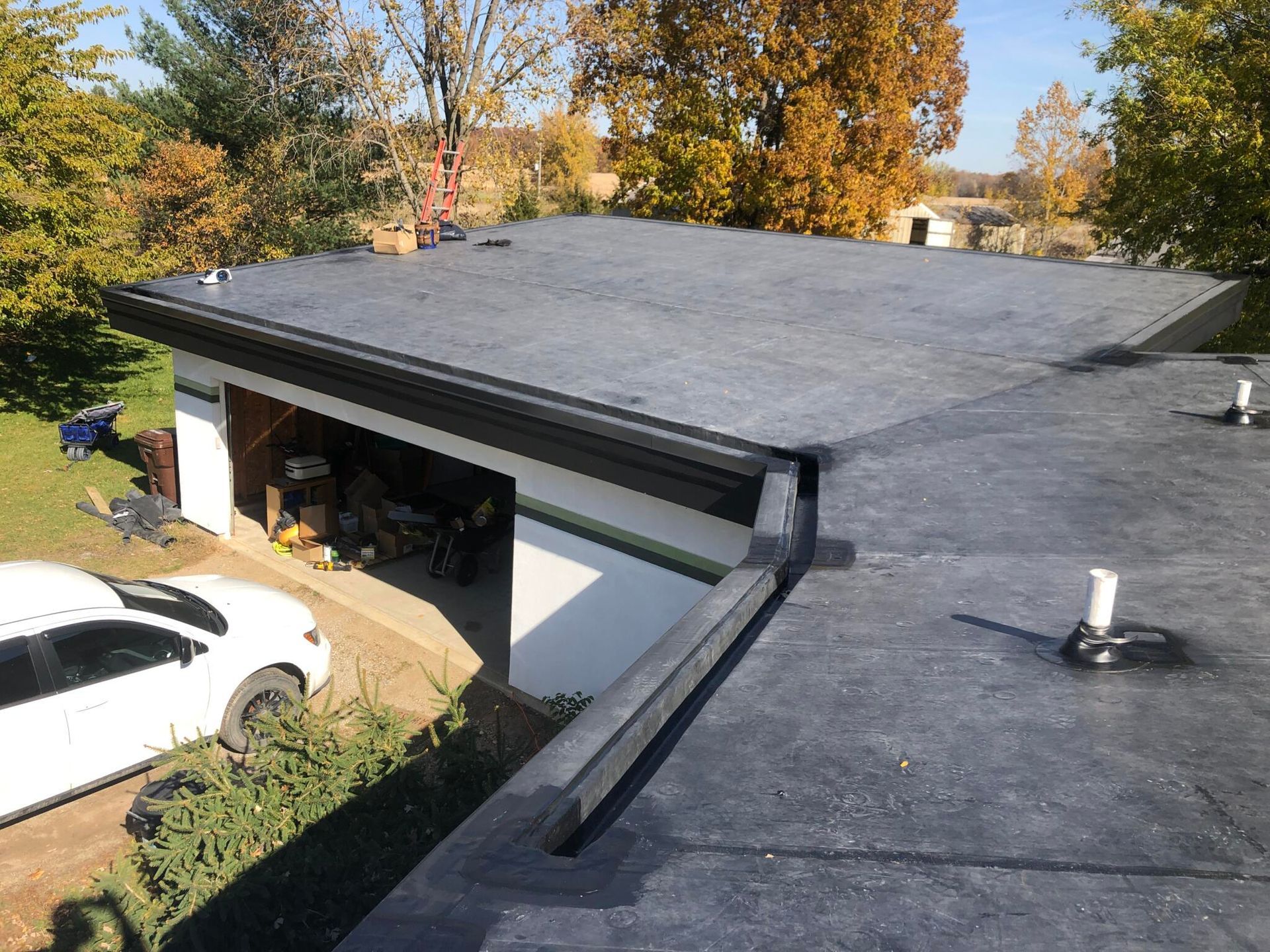 Flat, dark roof with garage; white car in driveway, surrounded by trees.