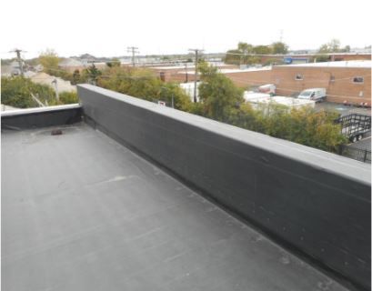 Flat, black roof with a low, dark wall along the edge, overlooking an urban landscape.