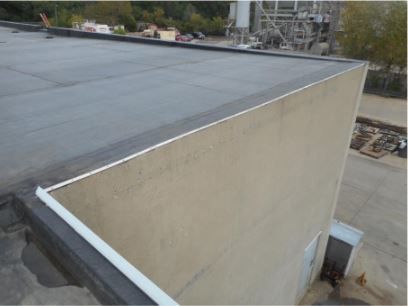 Flat roof with dark covering and white trim on a beige building exterior.