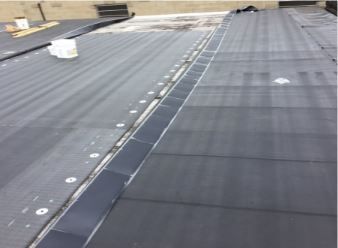 Black flat roof with a built-in gutter, showing sealant and fasteners.