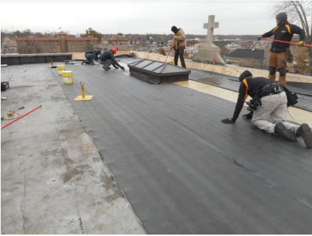 Construction workers installing a black roofing membrane on a building.