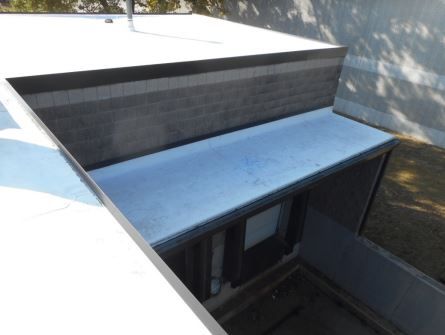Exterior building corner with a flat roof and dark brick wall, with a view into a lower section.