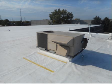 Rooftop HVAC unit on a white flat roof. A yellow safety grid is below the unit. Sunny day.