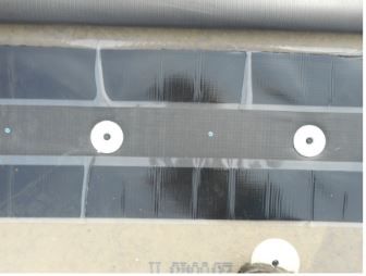 Close-up of black solar panels covered with clear plastic film, mounted on a surface, with white circular fasteners.