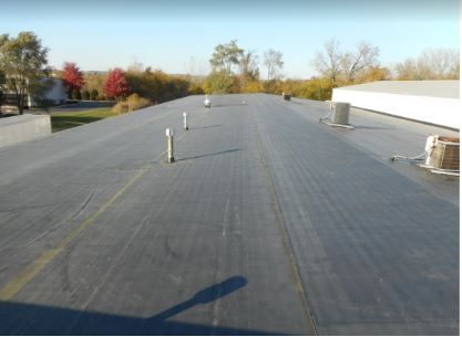 Black flat commercial roof with vents, HVAC unit, and a distant tree line.