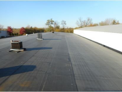 Flat, dark commercial roof with HVAC units under a clear sky.