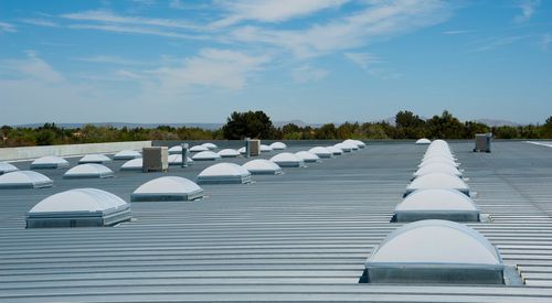 A flat, gray commercial roof with numerous white skylights under a blue sky.