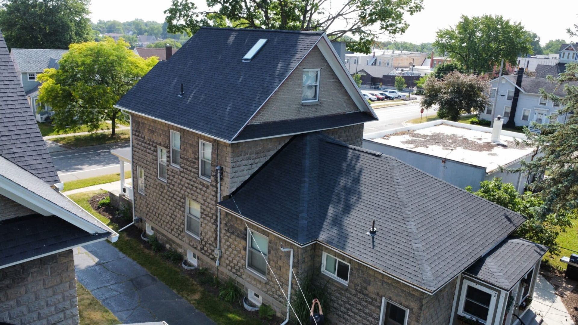 Two-story house with dark roof and light brick siding on a sunny day.