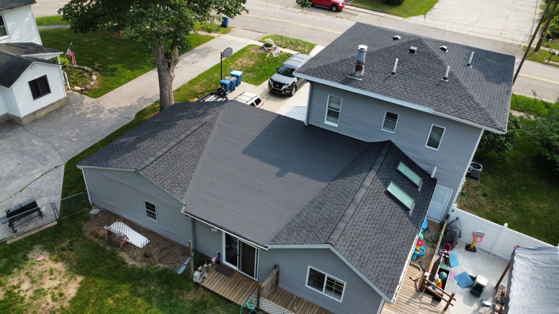 Aerial view of two-story gray house with dark roof and adjacent smaller building, located in a residential neighborhood.
